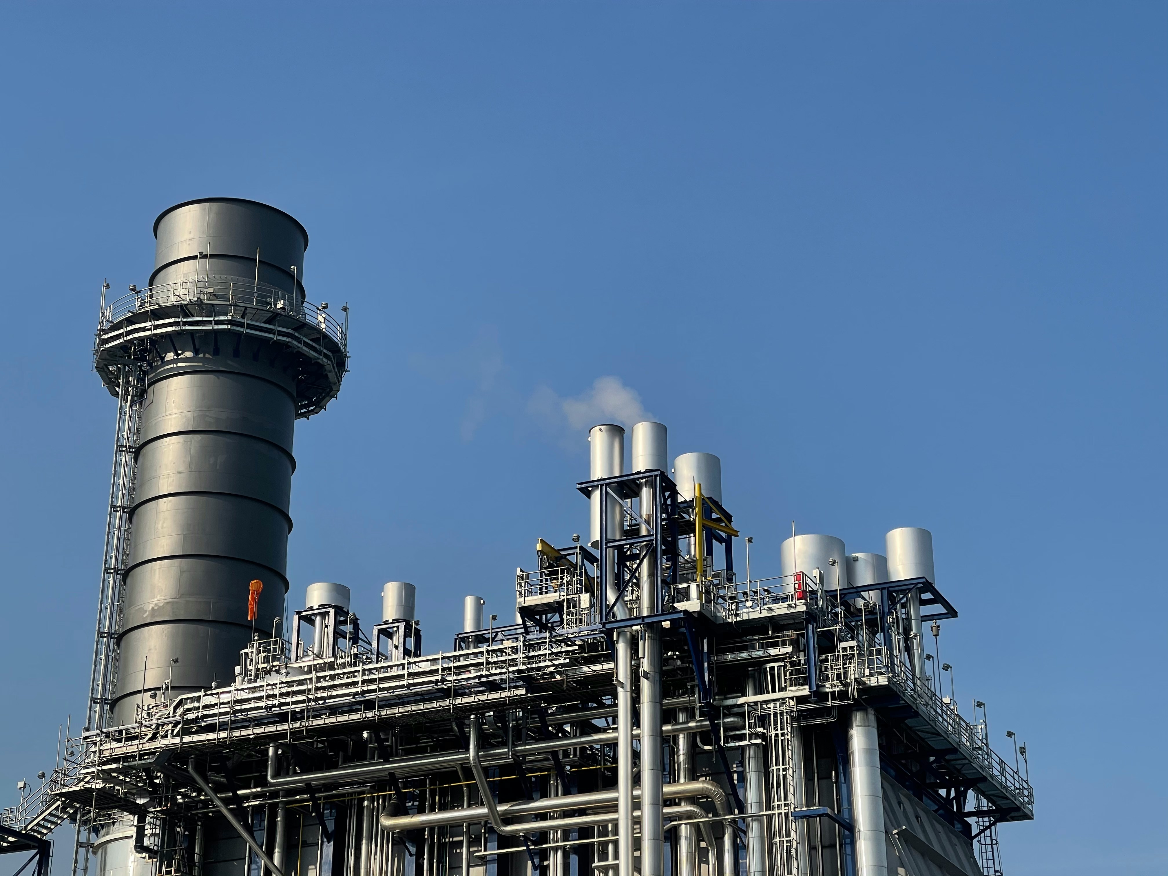 Industrial stack and process piping against a blue sky